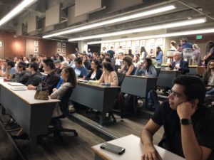 Photo of a classroom of people sitting at rows of desks for an ExplOrigins meeting