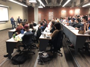Different angle of Photo of a classroom of people sitting at rows of desks for an ExplOrigins meeting